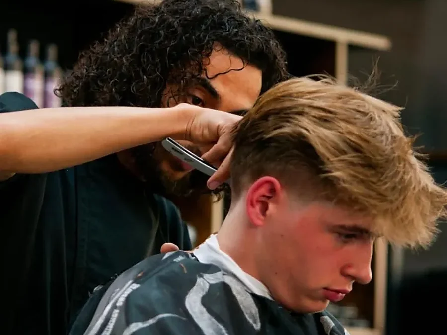 Barber knipt een blonde klant met schaar en kam